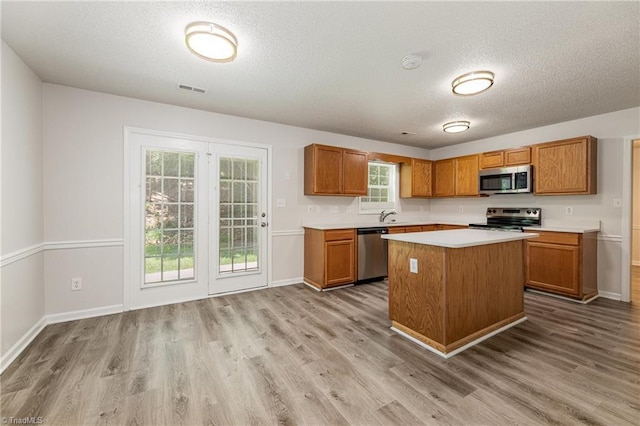 5207 Highland Oak Ct, Greensboro, NC 27410 - kitchen with stainless steel appliances, light countertops, wood finished floors, brown cabinetry, and a textured ceiling