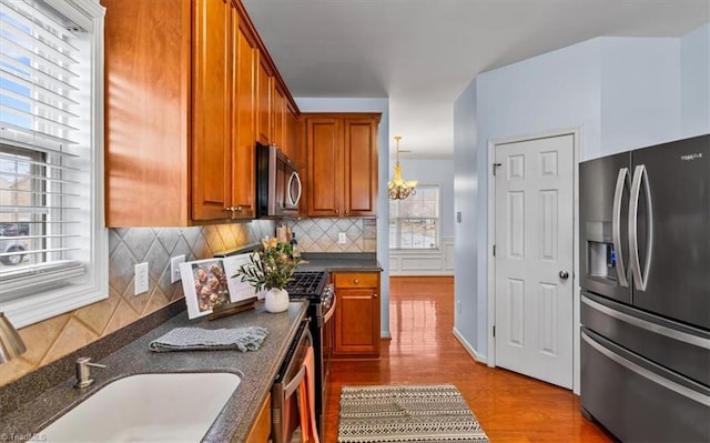 kitchen featuring brown cabinetry, decorative backsplash, wood finished floors, stainless steel appliances, and a sink