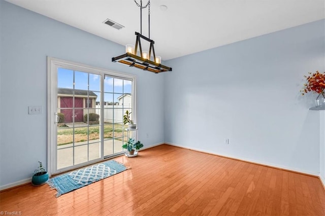 unfurnished dining area with baseboards, a notable chandelier, visible vents, and wood finished floors