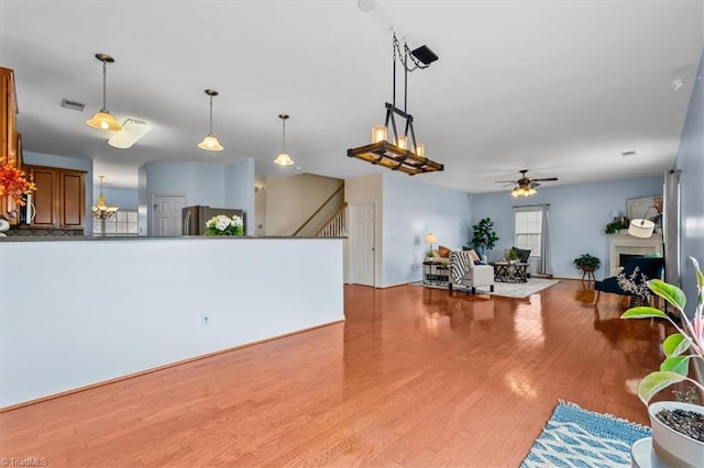 living area with a fireplace, visible vents, a ceiling fan, stairs, and light wood finished floors