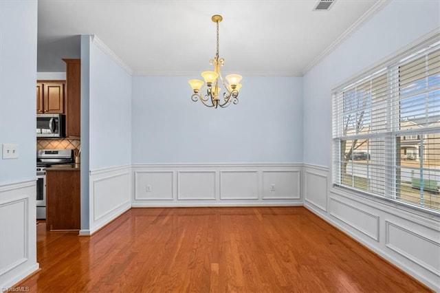 unfurnished dining area with an inviting chandelier, crown molding, and wood finished floors