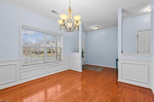 unfurnished dining area featuring visible vents, wainscoting, wood finished floors, an inviting chandelier, and a decorative wall