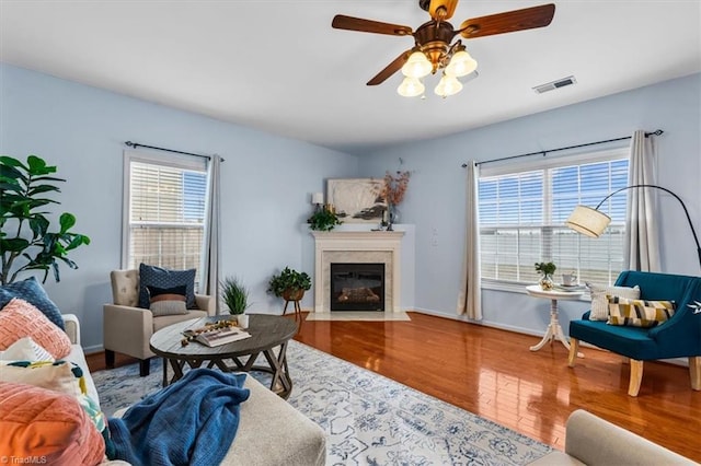 living area with ceiling fan, a fireplace with flush hearth, wood finished floors, visible vents, and baseboards