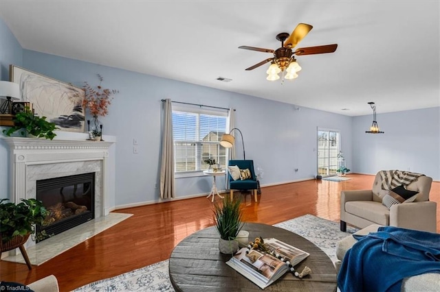 living area featuring a high end fireplace, a healthy amount of sunlight, visible vents, and wood finished floors