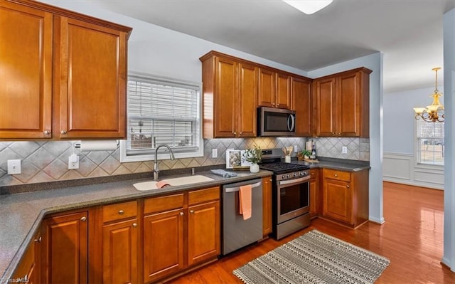 kitchen featuring stainless steel appliances, wood finished floors, a sink, brown cabinets, and dark countertops