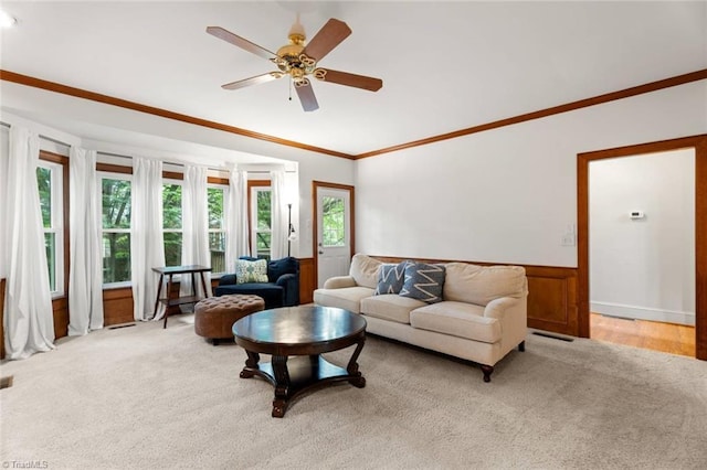 living room with ornamental molding, wainscoting, ceiling fan, and light colored carpet
