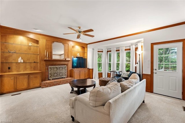 living room featuring crown molding, a brick fireplace, built in features, light colored carpet, and ceiling fan