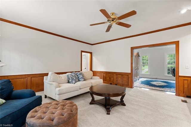 living room with a wainscoted wall, light carpet, crown molding, and a ceiling fan