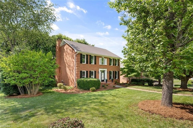 colonial-style house with a chimney, a front yard, and brick siding