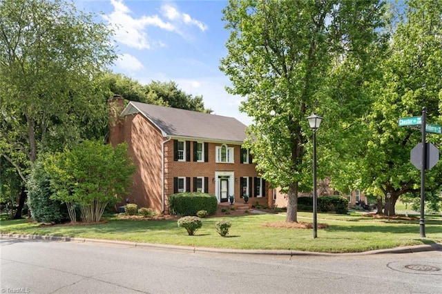colonial inspired home with brick siding, a chimney, and a front lawn