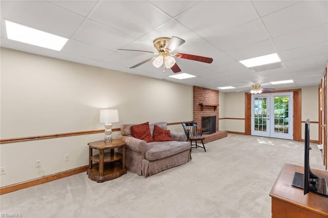 living area with ceiling fan, carpet floors, a fireplace, a drop ceiling, and french doors