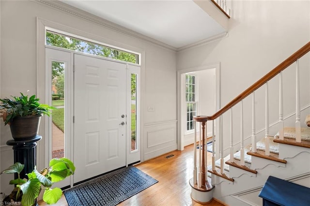 foyer entrance with stairway, light wood-style floors, ornamental molding, and a decorative wall