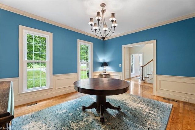 dining area featuring a chandelier, plenty of natural light, a wainscoted wall, ornamental molding, and stairway