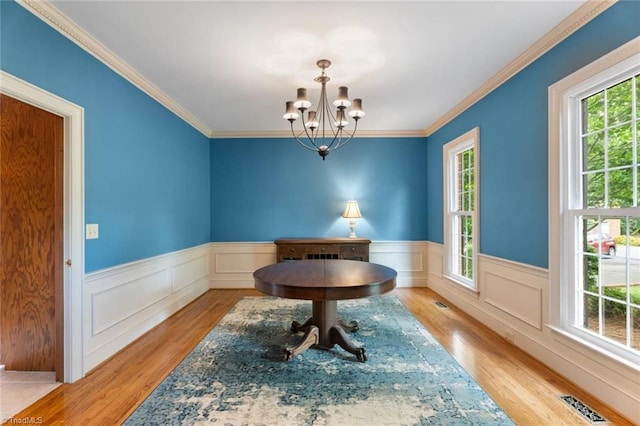 dining space featuring wood finished floors, a chandelier, a wainscoted wall, and ornamental molding
