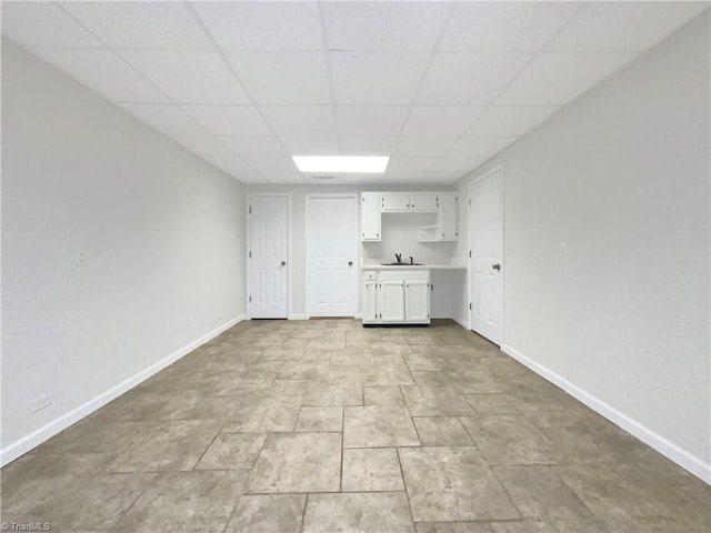 interior space with baseboards, a drop ceiling, and a sink