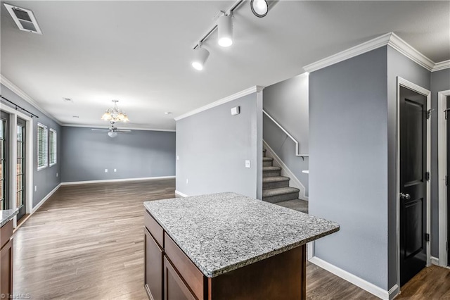 kitchen with visible vents, a center island, baseboards, ornamental molding, and wood finished floors