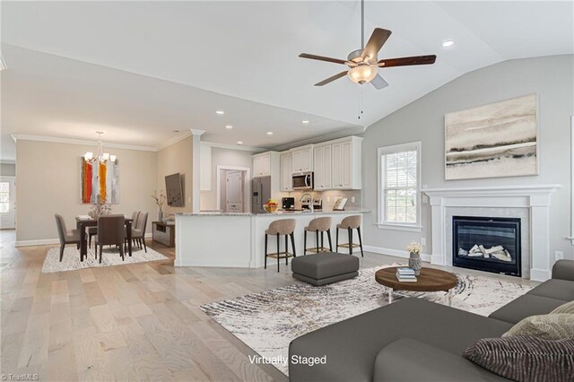 living room with light hardwood / wood-style flooring, vaulted ceiling, ceiling fan with notable chandelier, and ornamental molding