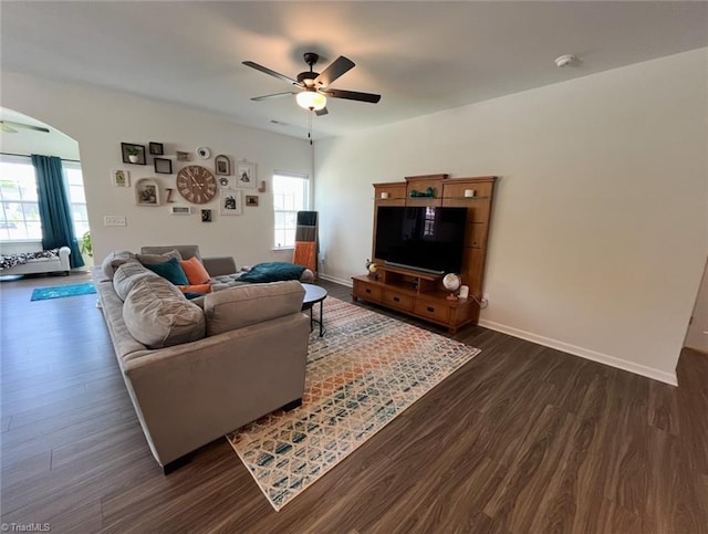 living room featuring baseboards, arched walkways, dark wood-style flooring, and ceiling fan