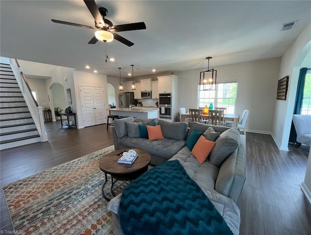 living area with visible vents, arched walkways, baseboards, ceiling fan with notable chandelier, and dark wood-type flooring