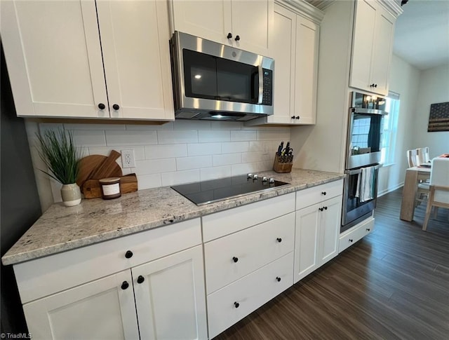 kitchen featuring appliances with stainless steel finishes, decorative backsplash, dark wood-style flooring, and white cabinetry