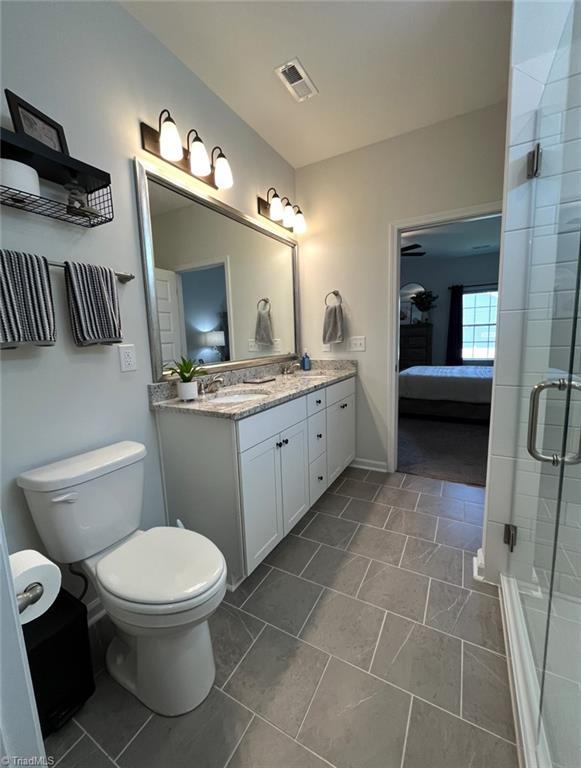 bathroom with double vanity, toilet, a shower stall, ensuite bathroom, and visible vents