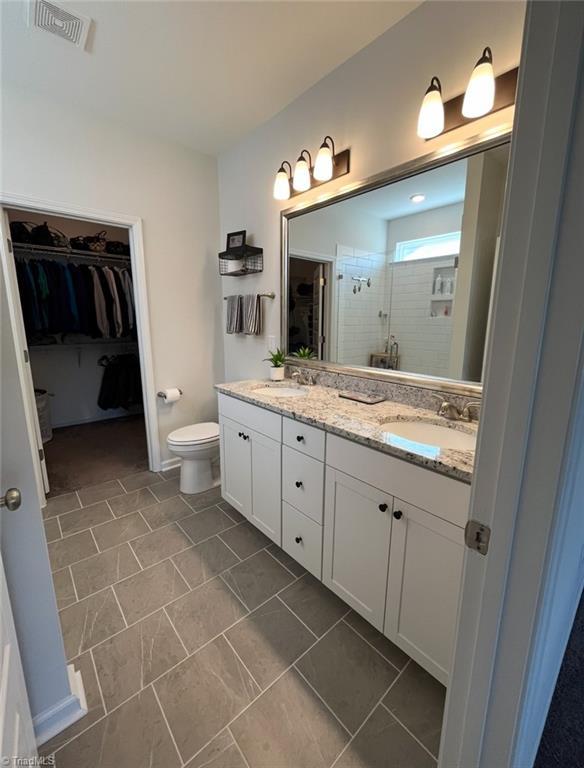 full bathroom with double vanity, visible vents, a stall shower, a sink, and a spacious closet