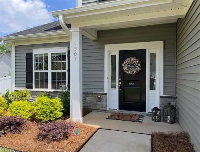 view of exterior entry featuring a shingled roof and stone siding
