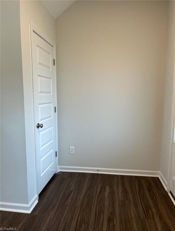 spare room featuring baseboards and dark wood-type flooring