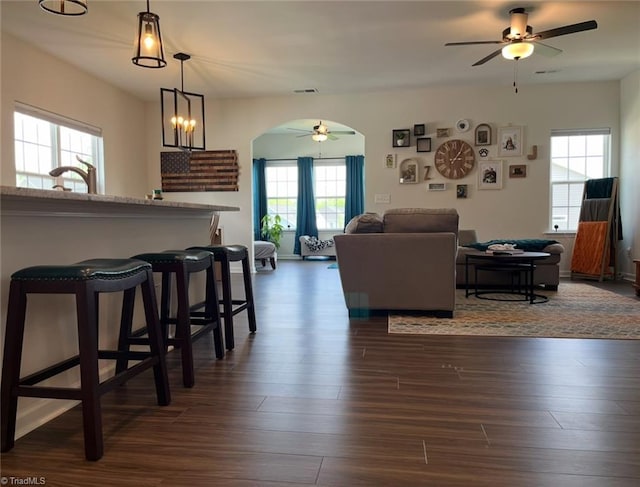 living area featuring arched walkways, ceiling fan, and dark wood finished floors