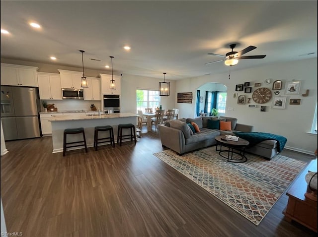 living area with a ceiling fan, baseboards, dark wood-type flooring, recessed lighting, and arched walkways