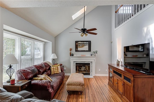 living room featuring ceiling fan, high vaulted ceiling, a skylight, and light hardwood / wood-style flooring