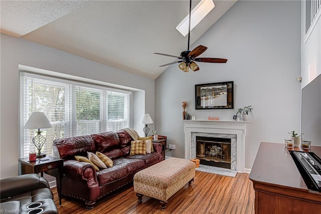 living room featuring a skylight, hardwood / wood-style floors, ceiling fan, high vaulted ceiling, and a premium fireplace