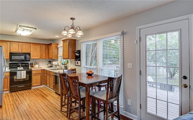 kitchen with a textured ceiling, a chandelier, black appliances, light hardwood / wood-style floors, and decorative light fixtures