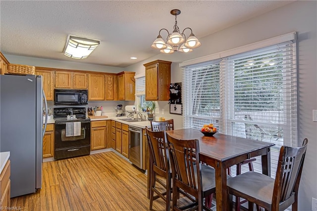 kitchen featuring hanging light fixtures, an inviting chandelier, light wood-type flooring, black appliances, and sink