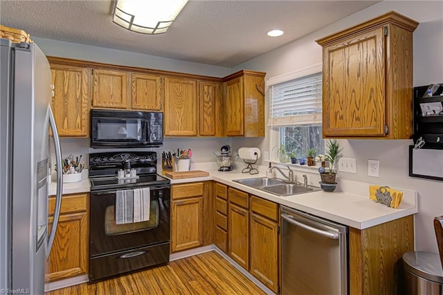 kitchen featuring sink, black appliances, light hardwood / wood-style flooring, and a textured ceiling