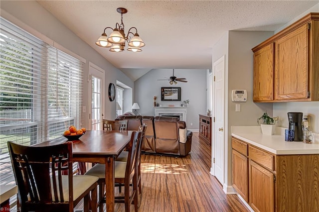 dining space with a textured ceiling, vaulted ceiling, ceiling fan with notable chandelier, and hardwood / wood-style floors