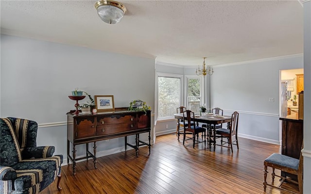 dining area with a textured ceiling, wood-type flooring, ornamental molding, and a chandelier