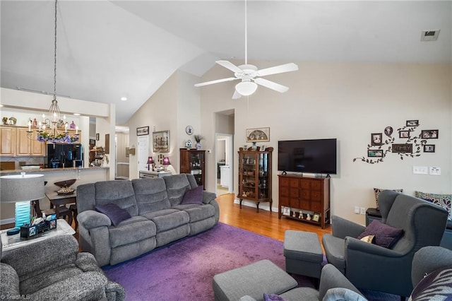 living room with visible vents, high vaulted ceiling, wood finished floors, and ceiling fan with notable chandelier