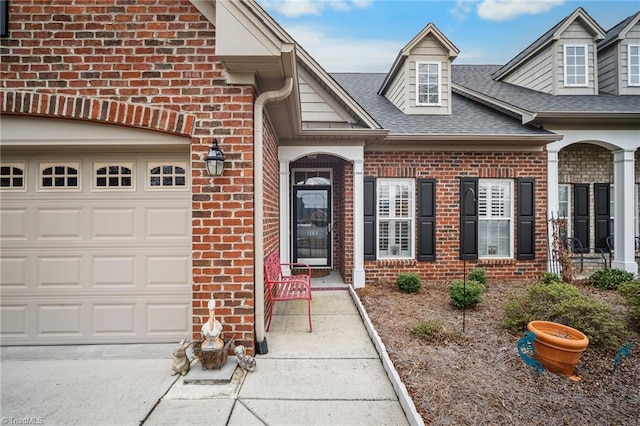 doorway to property featuring a garage, brick siding, and roof with shingles