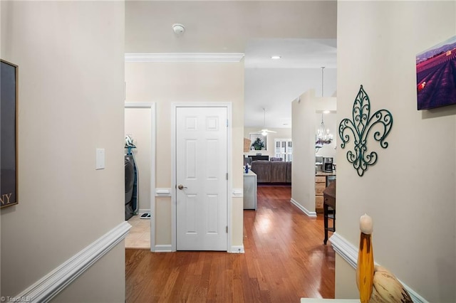 hallway with crown molding, a notable chandelier, wood finished floors, and baseboards