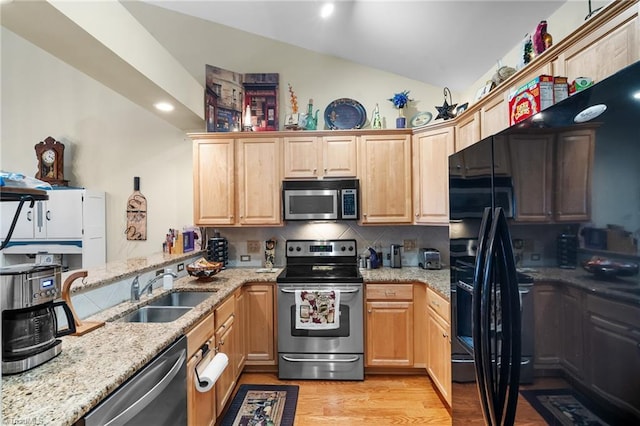 kitchen with light stone countertops, a sink, vaulted ceiling, appliances with stainless steel finishes, and light wood-type flooring