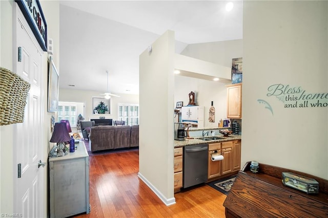 kitchen featuring a ceiling fan, a sink, stainless steel dishwasher, light wood finished floors, and light stone countertops