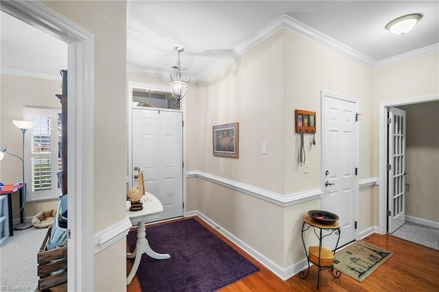 hallway featuring an inviting chandelier, wood finished floors, baseboards, and ornamental molding