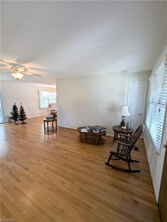 living area with ceiling fan, light hardwood / wood-style flooring, and a textured ceiling