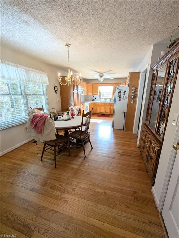 dining area with hardwood / wood-style flooring, plenty of natural light, ceiling fan with notable chandelier, and a textured ceiling