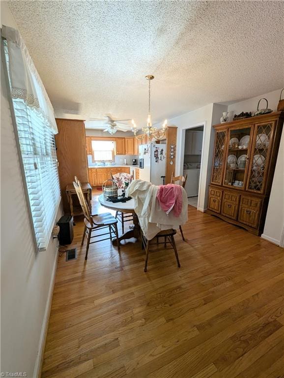 dining room with hardwood / wood-style floors, ceiling fan with notable chandelier, a textured ceiling, and washer / clothes dryer