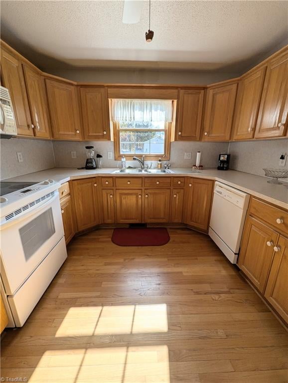 kitchen with a textured ceiling, light wood-type flooring, white appliances, and sink