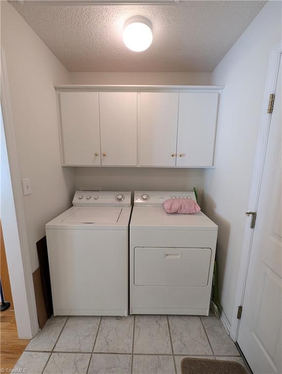 clothes washing area with cabinets, a textured ceiling, and independent washer and dryer