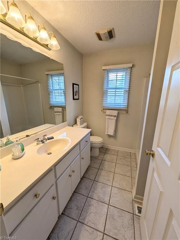 bathroom with a shower, vanity, a textured ceiling, and toilet