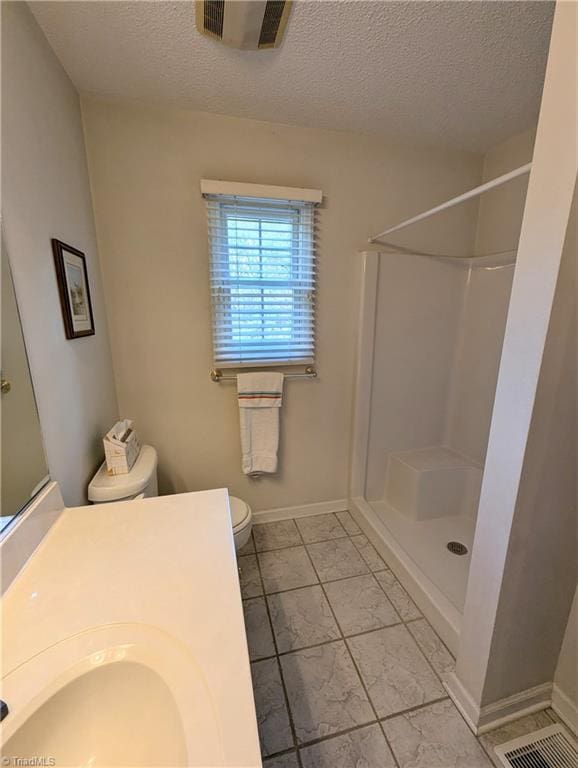 bathroom featuring a shower, a textured ceiling, toilet, and sink